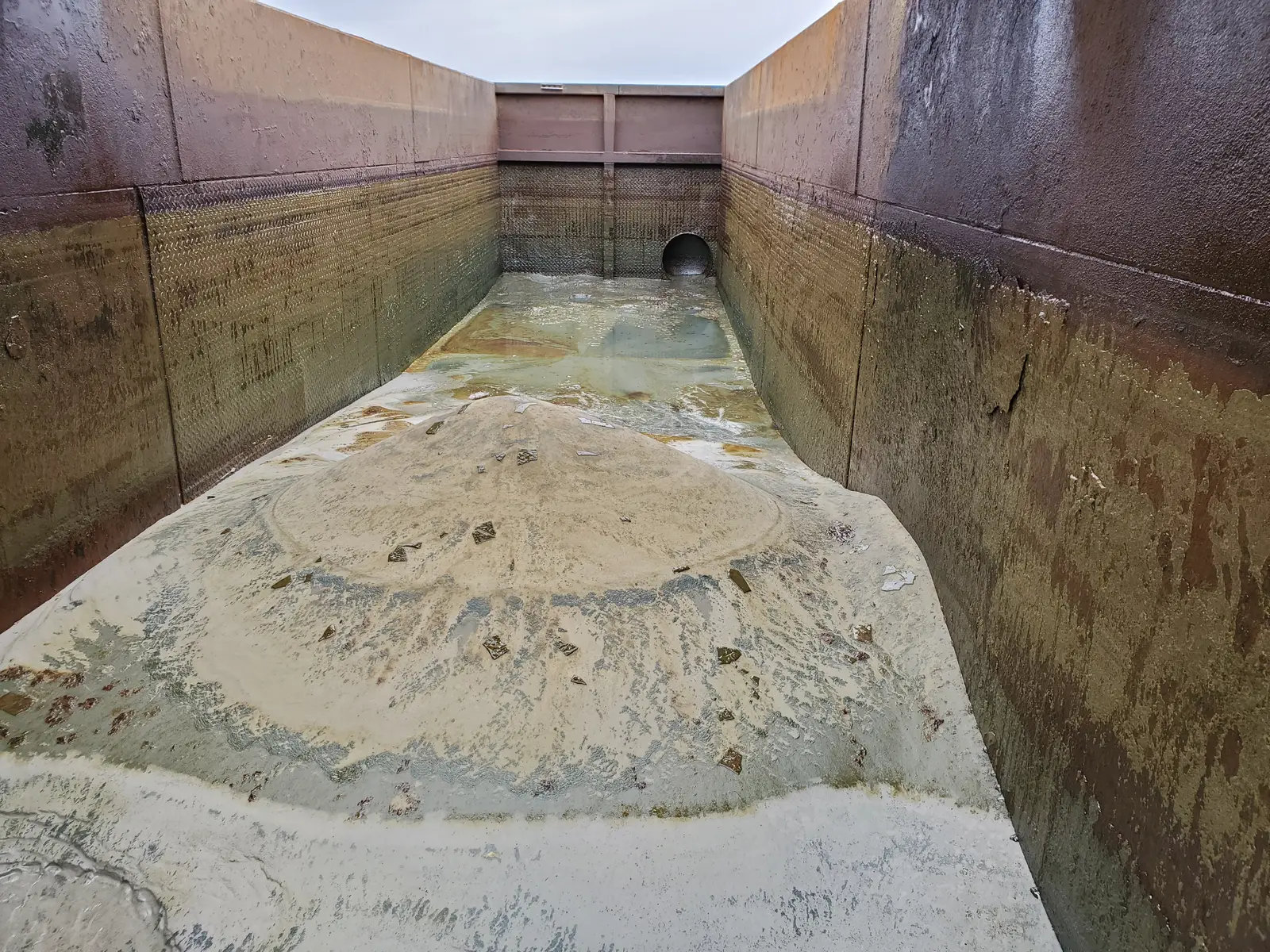 Sand and residual fluid mounded in the bottom of a steel-walled collection pit, waiting to be pumped and hauled off