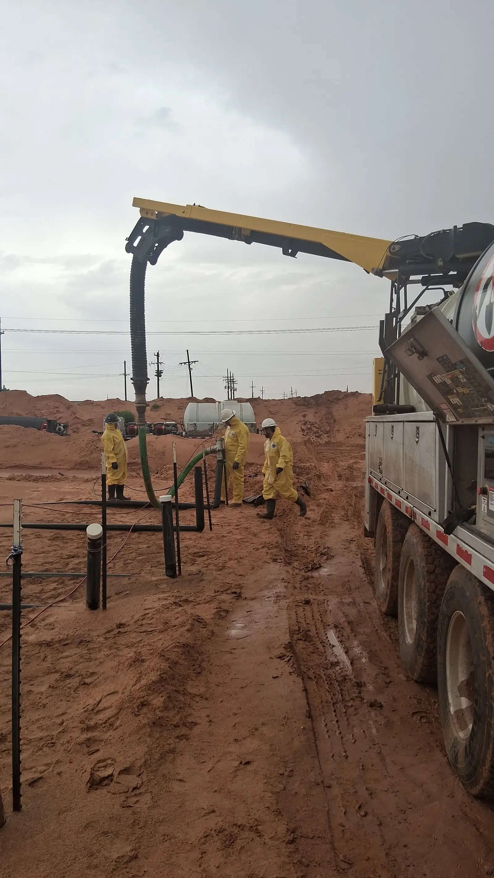 Three Gentex crew members in full chemical suits and hard hats working a line with the vacuum boom overhead