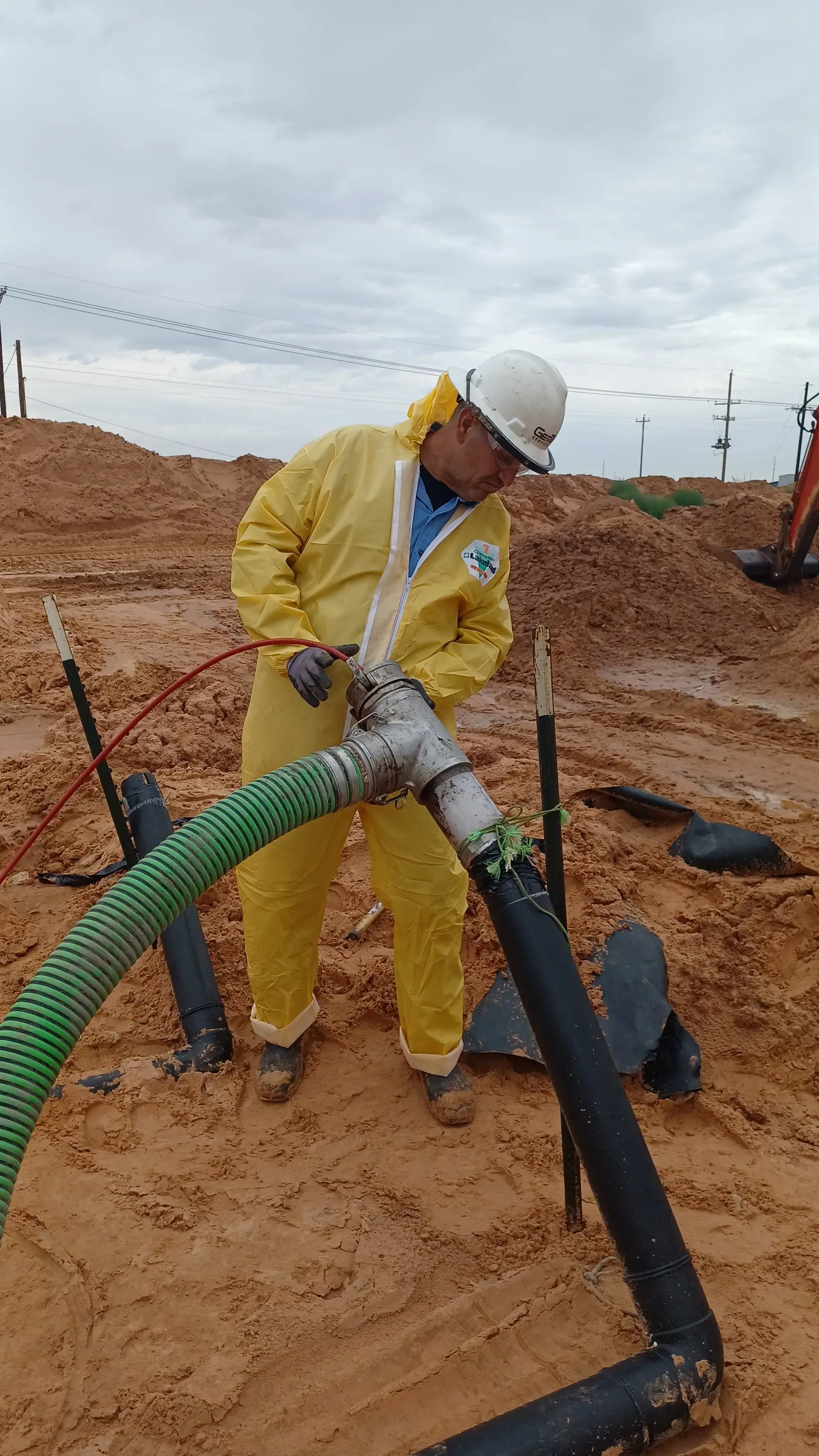 A Gentex operator in a chemical suit, hard hat and gloves feeding the jetting hose into a line at a wellsite
