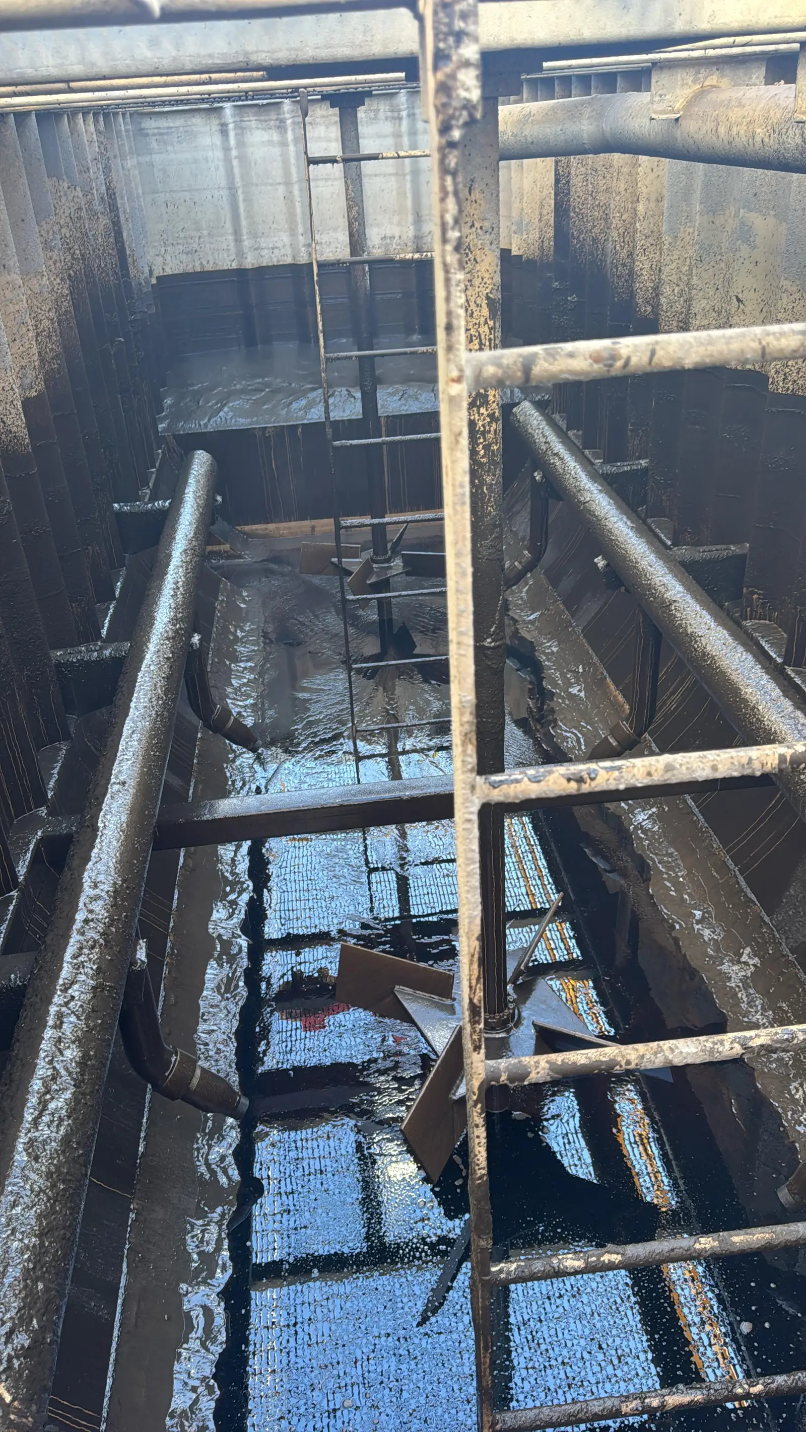 Inside a mixer before cleaning: black product coating the shell, the internal bracing and the agitator, with sludge pooled across the floor