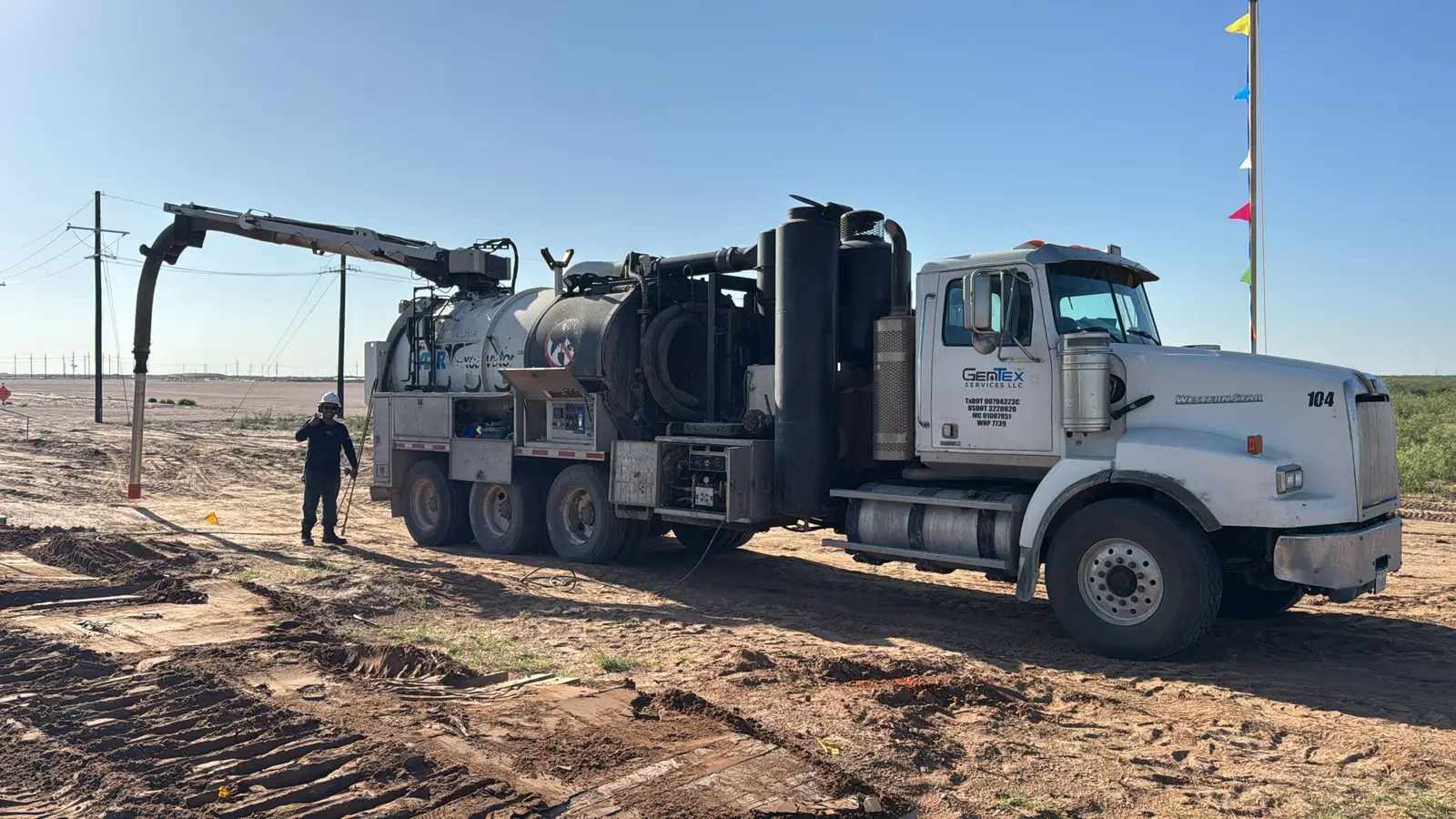 A Gentex vacuum truck set up at a dig with the boom hose down, an operator on the ground working alongside it