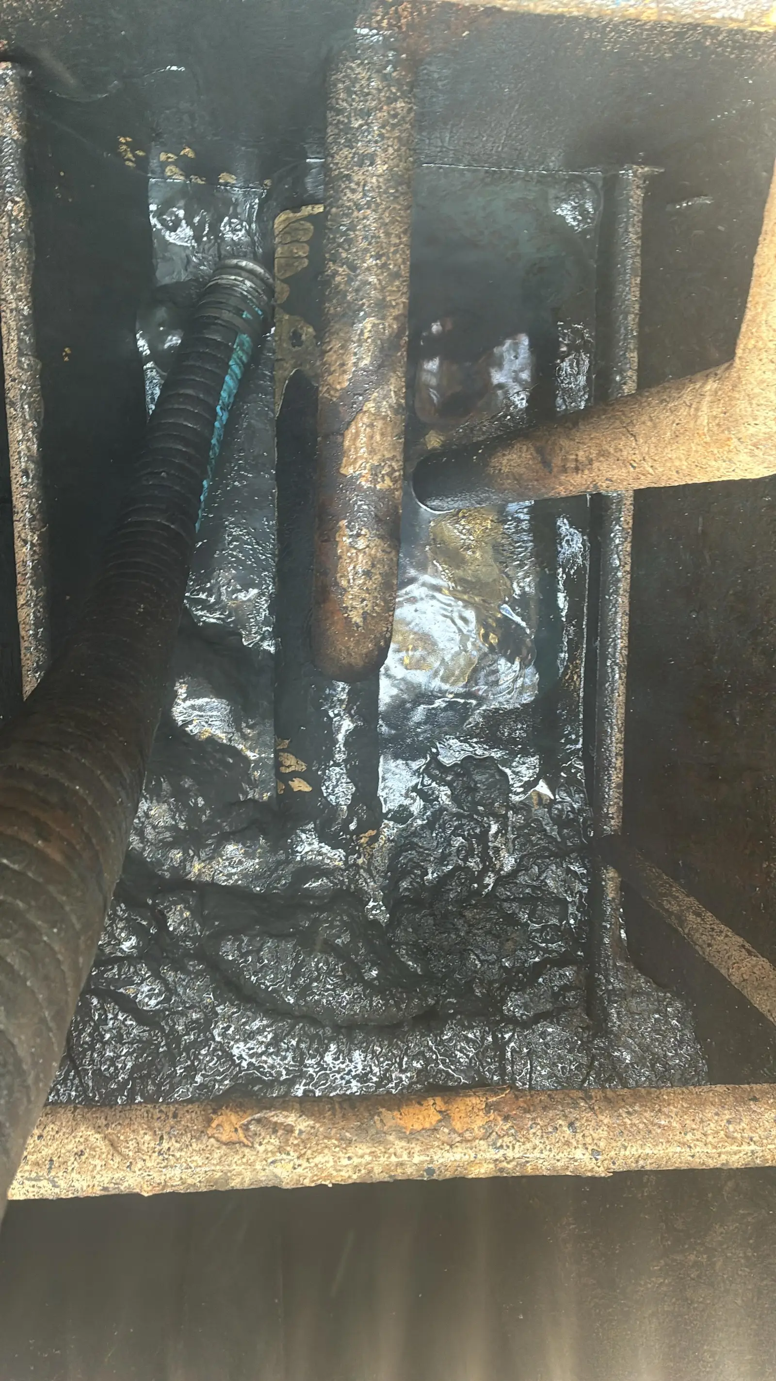 Inside a rig pit before clean-out: black sludge coating the floor, the bracing and the suction line