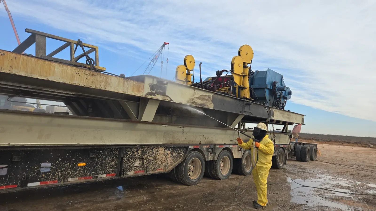 A Gentex operator washing down rig beams and drawworks on a lowboy, mud coming off the steel in a spray