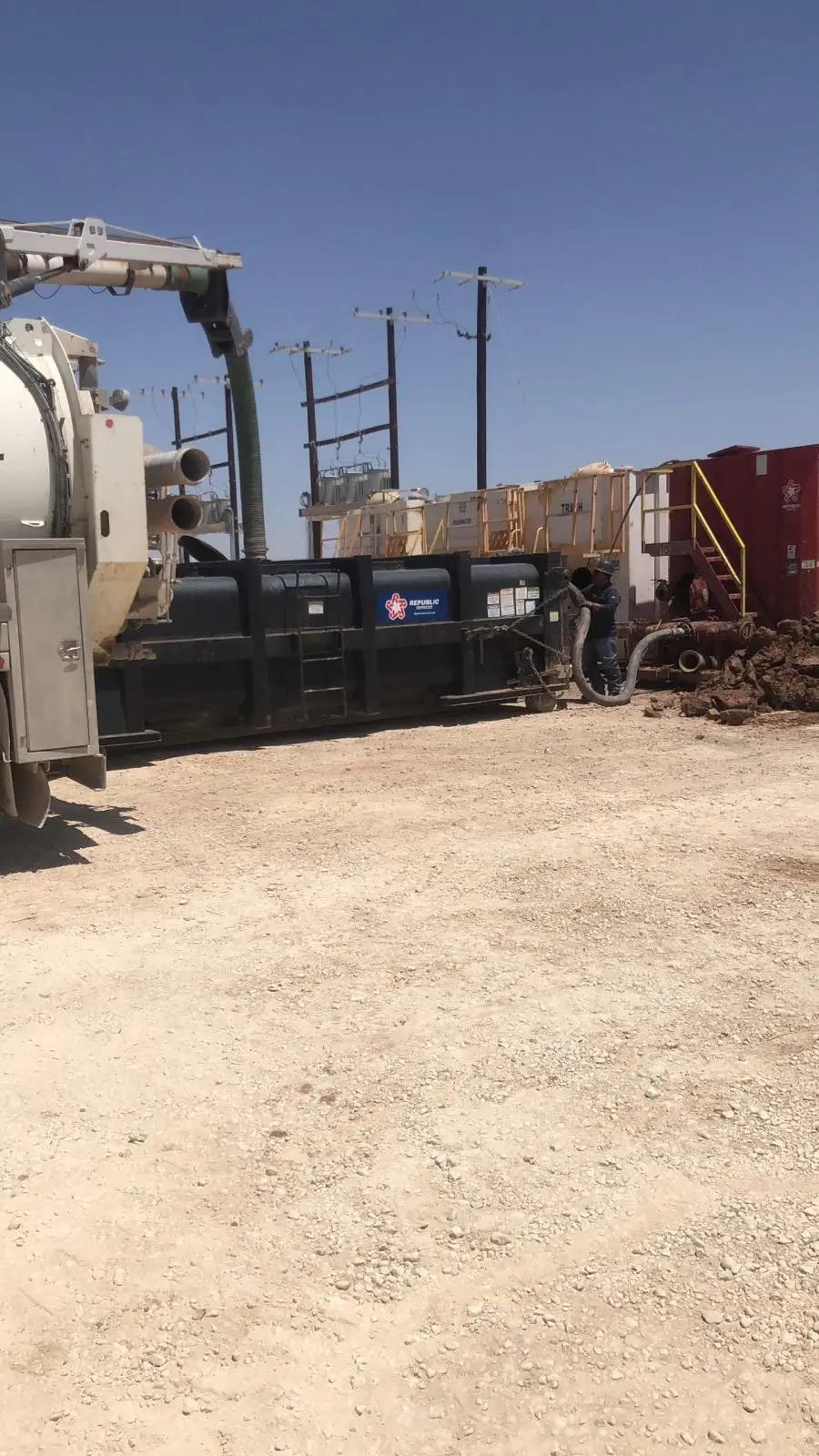 Gentex vacuum truck offloading into a roll-off box on location while a crew member handles the discharge hose