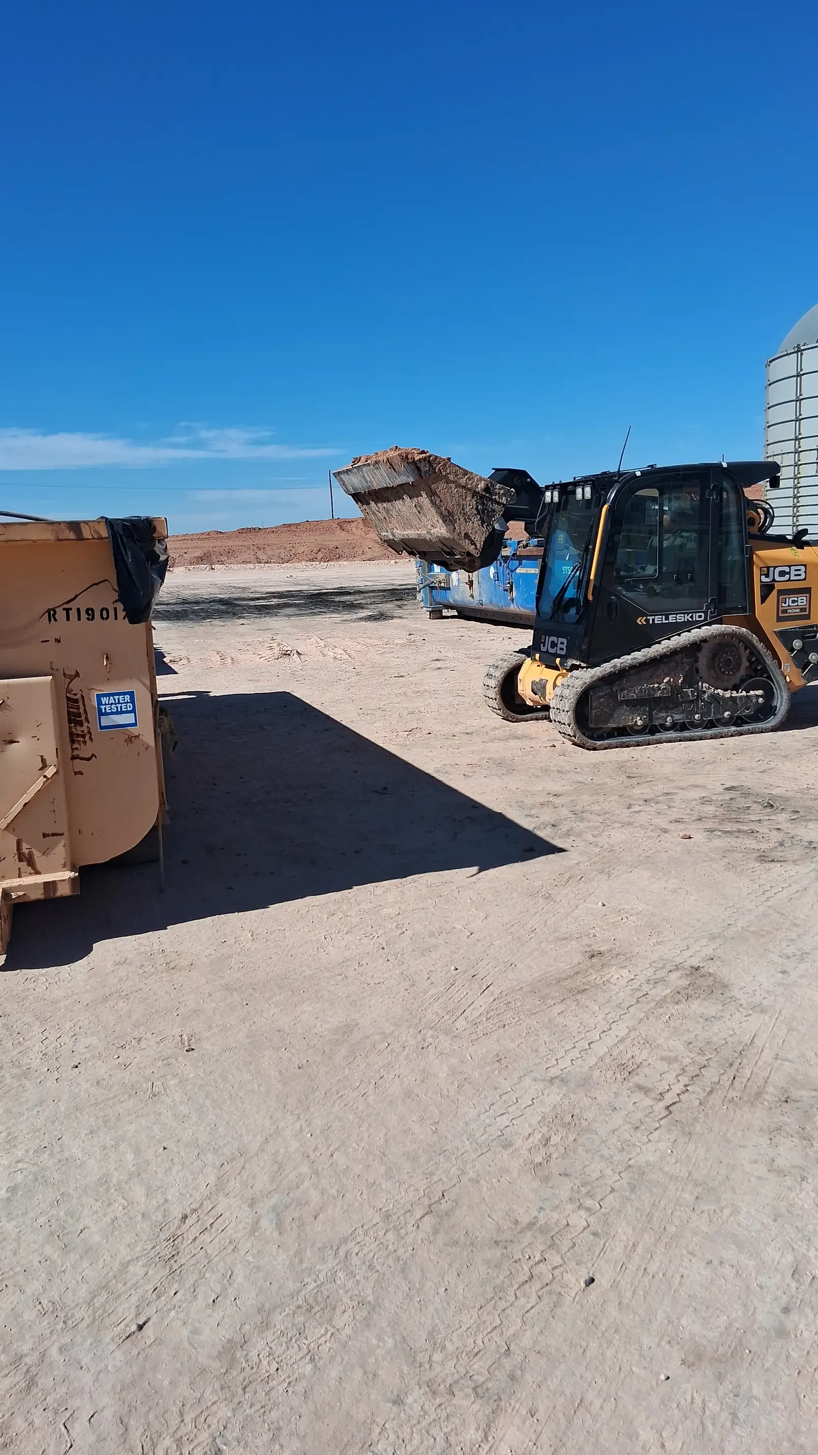 A tracked skid steer with a loaded bucket raised beside a roll-off box on a Gentex job site